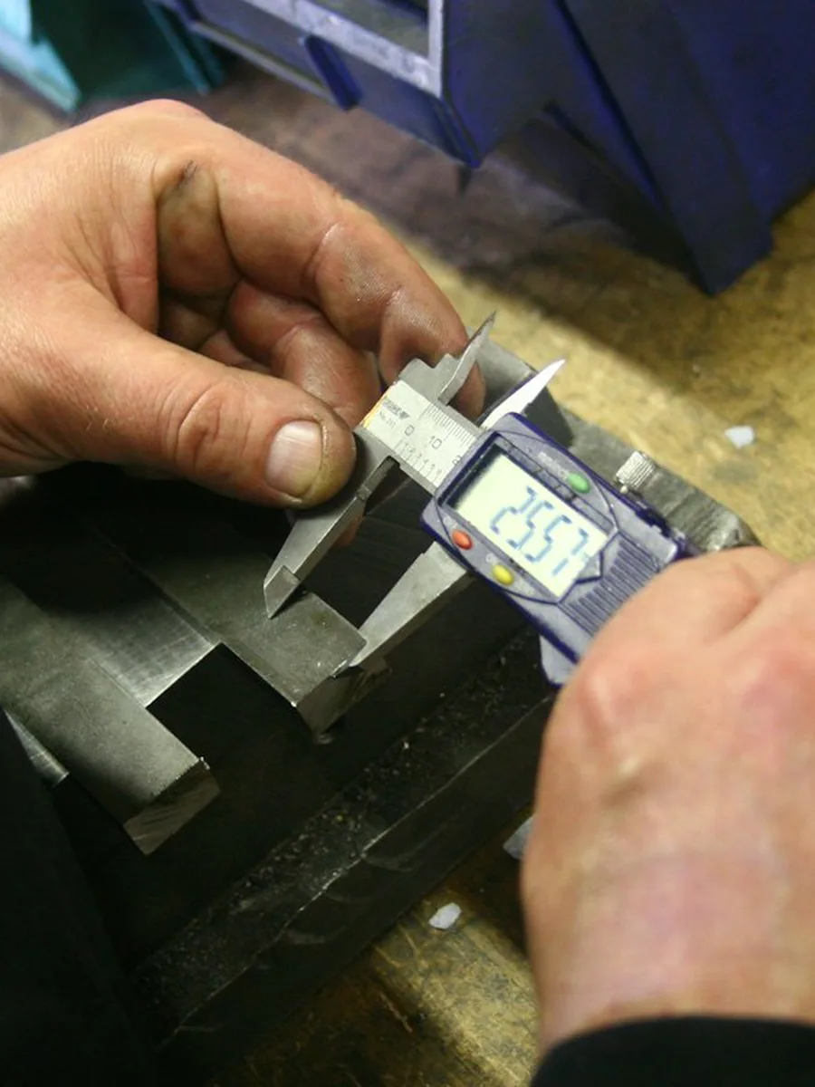 Hands measuring a metal part with a digital caliper